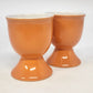 Pair of orange ceramic egg cups with white interiors and pedestal bases