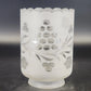 Decorative glass candle holder with floral cutout design on a dark background