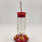 Clear glass hummingbird feeder with red base and six yellow flower ports