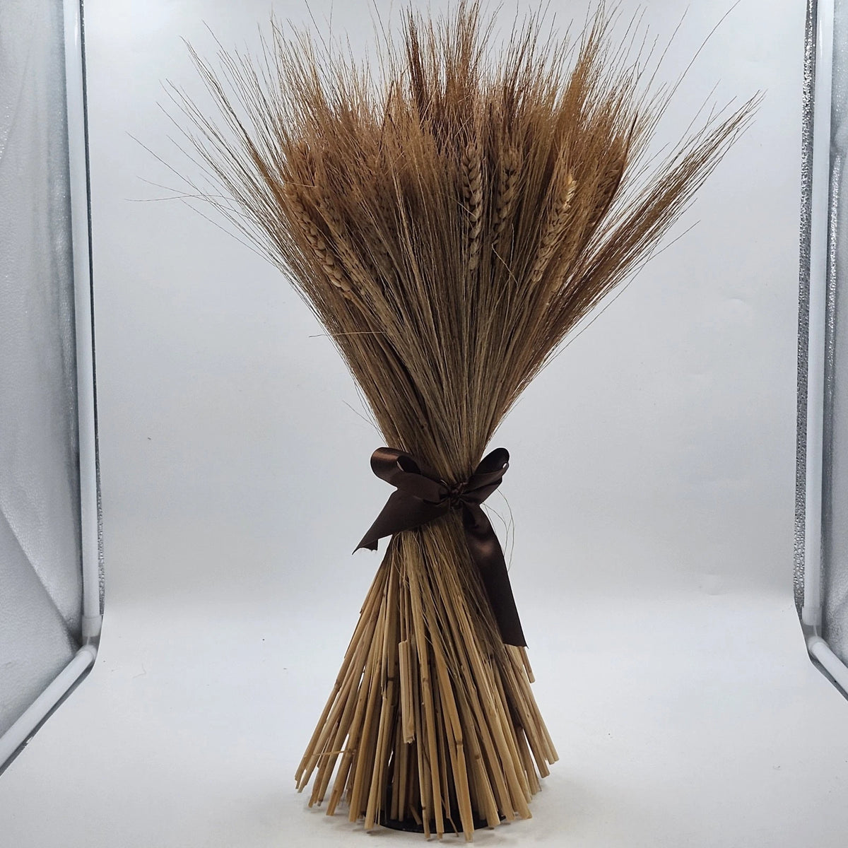 Fan-shaped dried wheat bundle with brown ribbon on tabletop