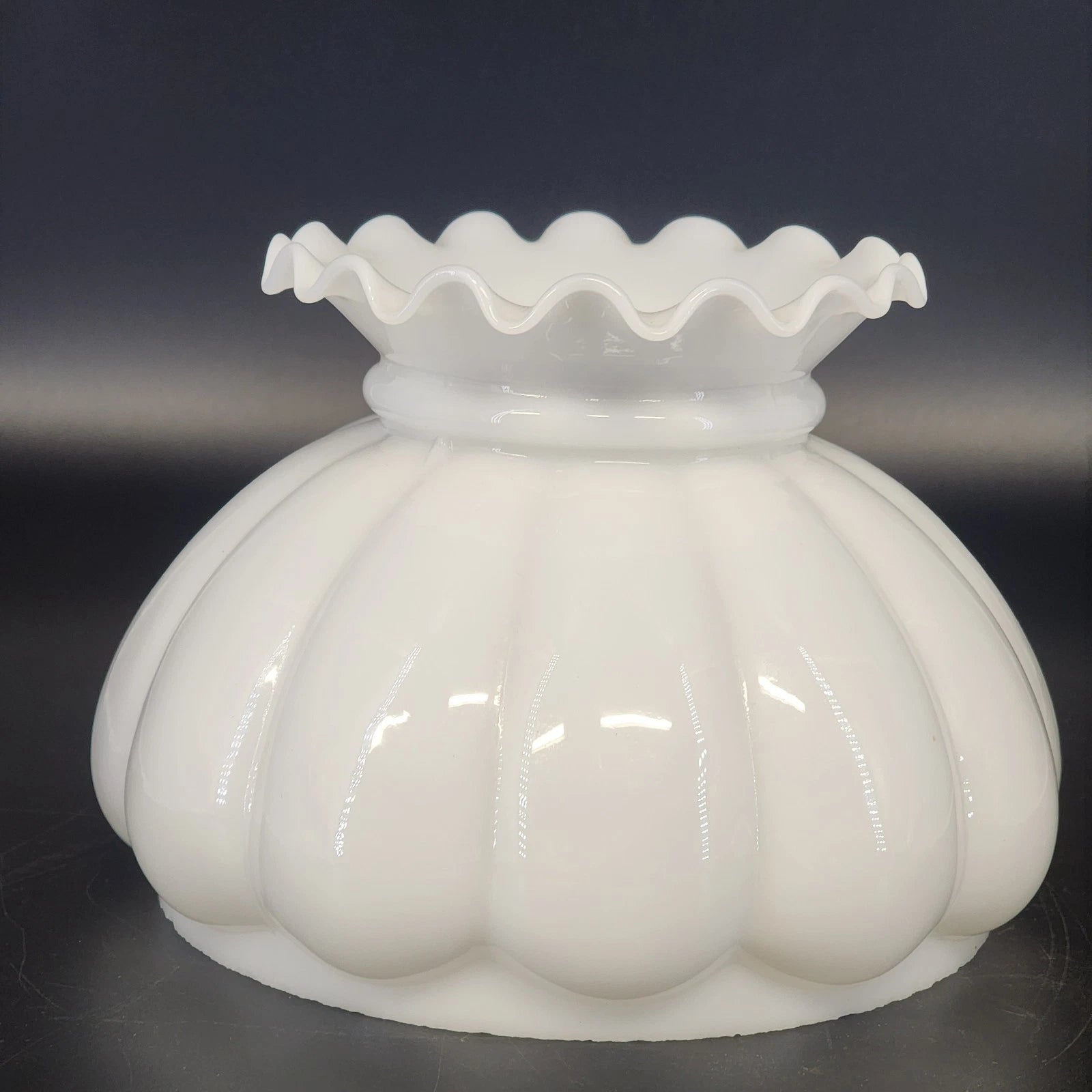 White glass lamp shade with ruffled top on a dark background