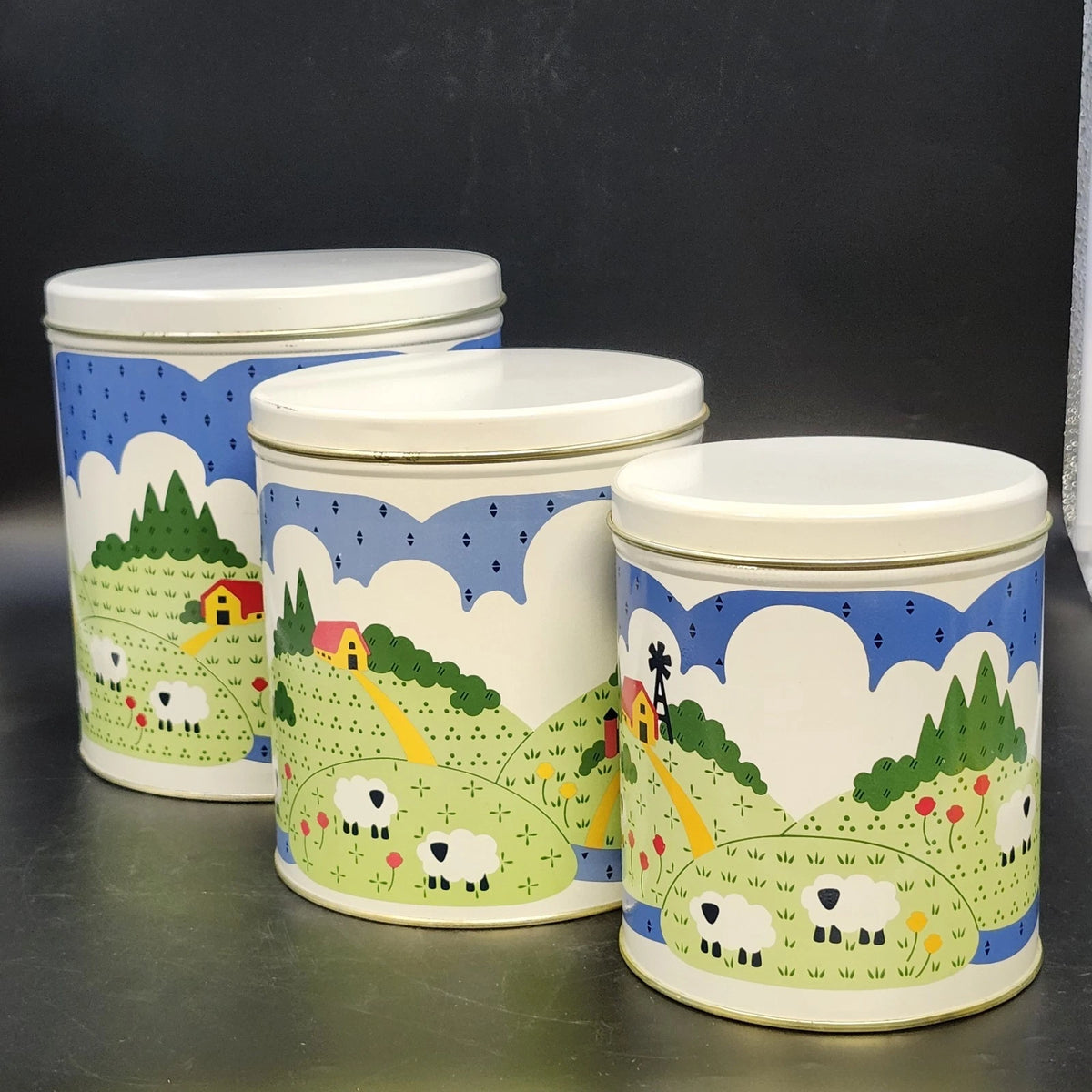 Vintage 1982 Nina nesting tin canister set of 3 with colorful farm scenes and cream lids.