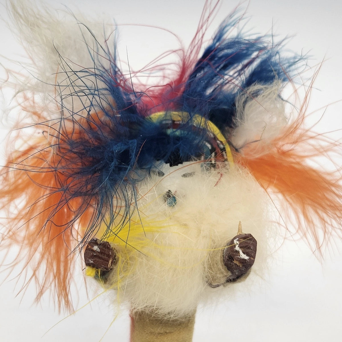 Handmade folk art figure with colorful feathers and rustic wood base