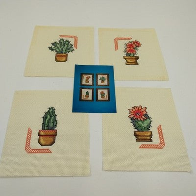 Set of four completed desert plant cross stitch designs on white Aida cloth