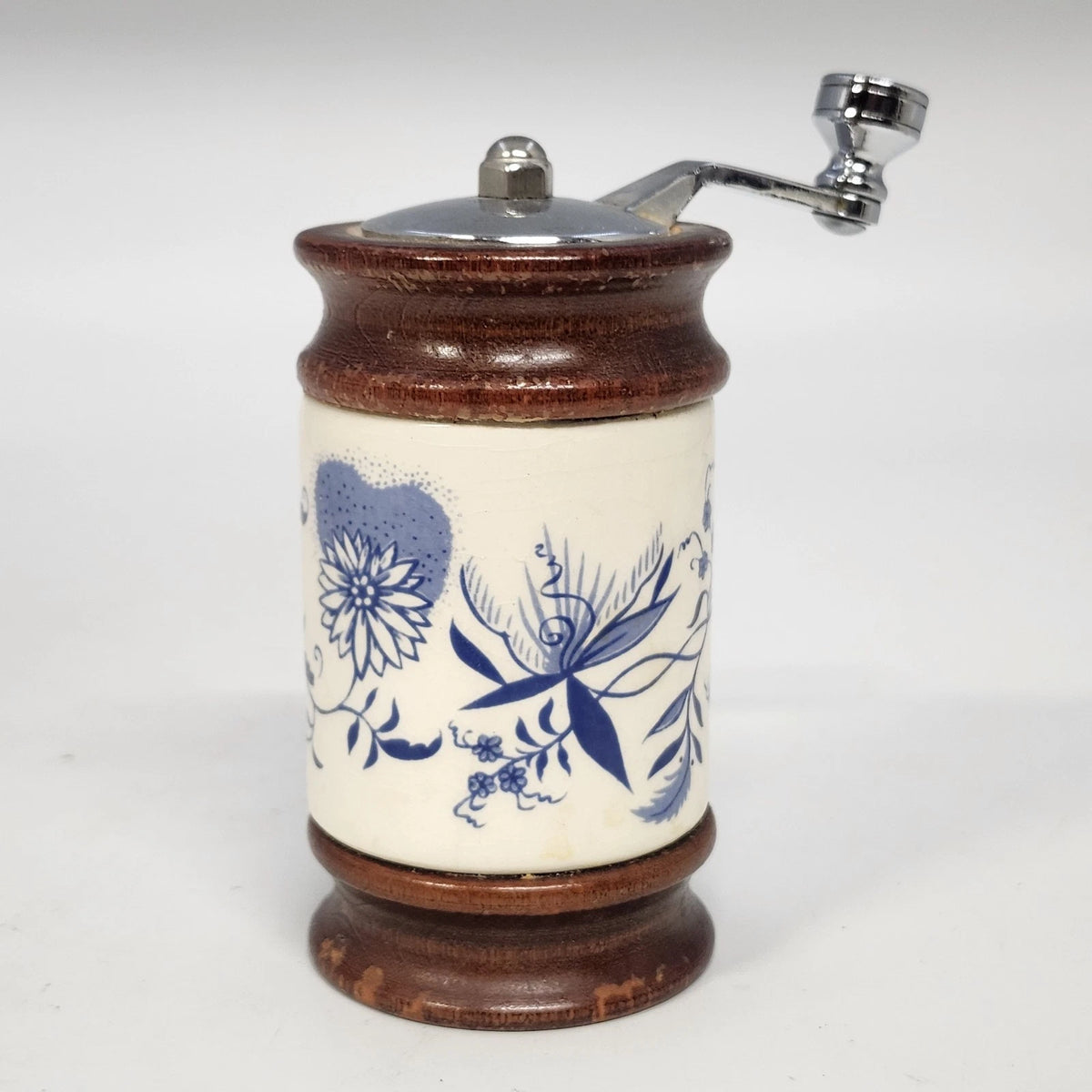 Vintage cream porcelain pepper grinder with blue floral designs, wooden top and base, and metal hand crank.