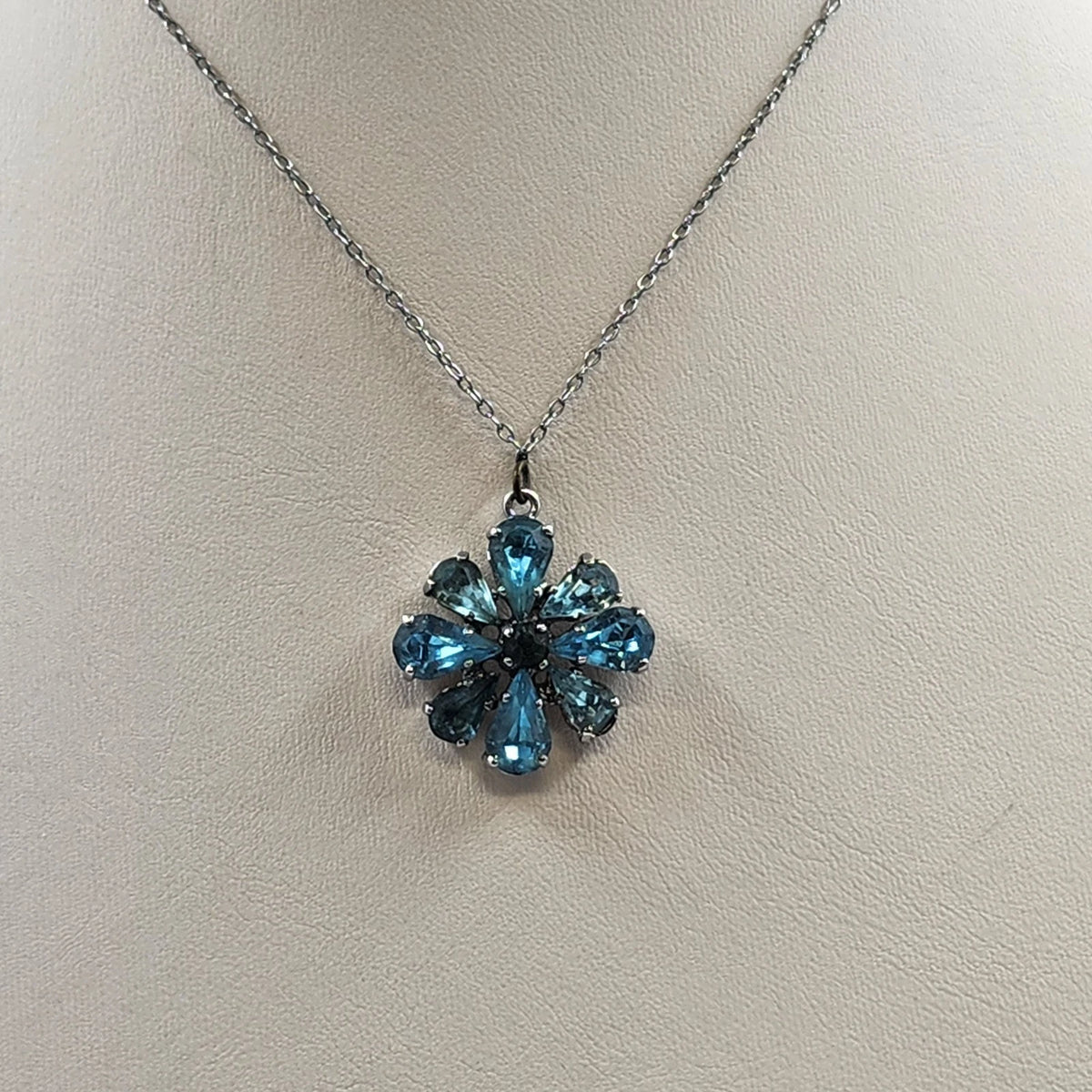 Silver-tone necklace with a flower pendant featuring faceted blue teardrop stones and a dark center.
