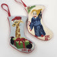 Set of two vintage needlepoint Christmas stocking ornaments featuring a Santa hat giraffe and a blue-robed angel