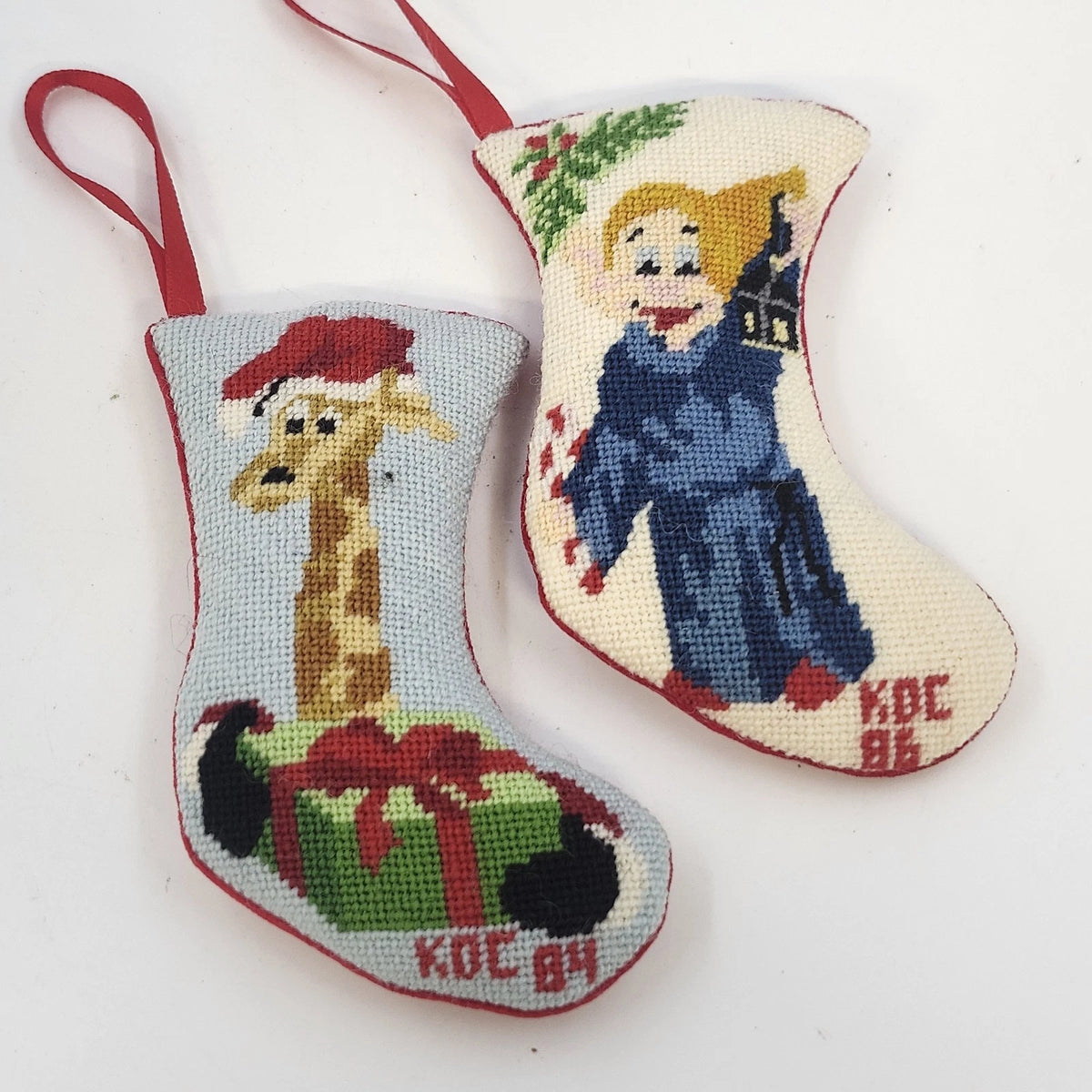 Set of two vintage needlepoint Christmas stocking ornaments featuring a Santa hat giraffe and a blue-robed angel