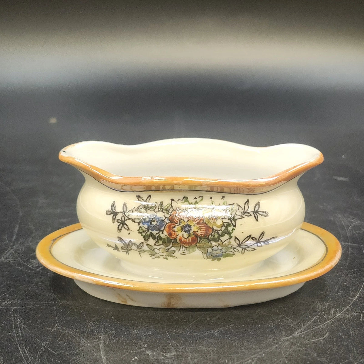 Vintage porcelain gravy boat with floral design, underplate, and orange gold trim
