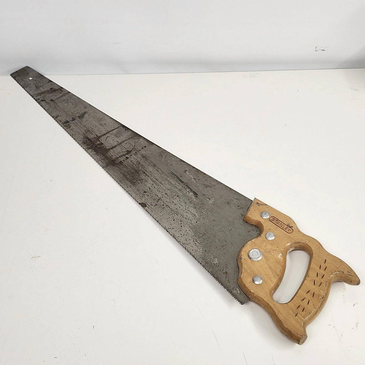 Vintage Stanley 26-inch crosscut hand saw with aged steel blade, shaped wooden handle with decorative incised details, Stanley medallion, and hanging hole.