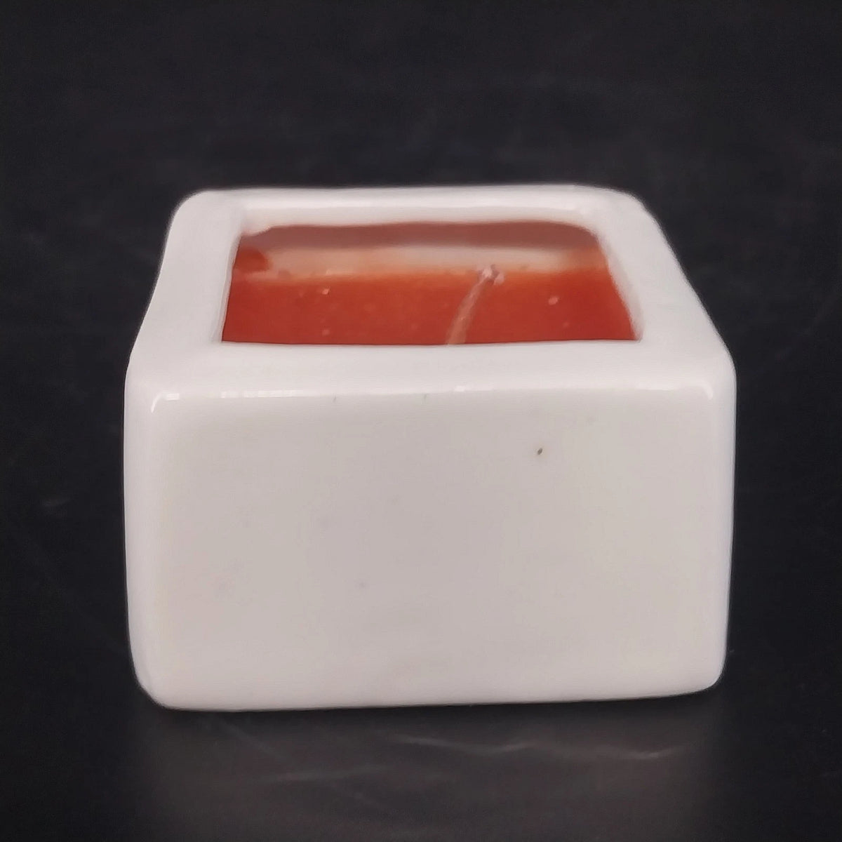 White ceramic square container candle with recessed red wax and single wick